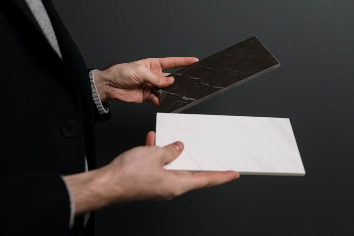 Close-up of hands holding two contrasting marble and stone tiles.